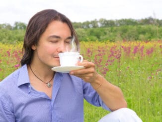 Portrait of young happy smiling man drinking coffee or tea outdoors