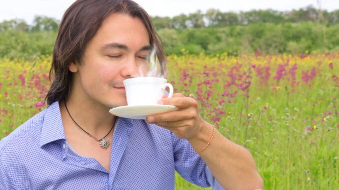 Portrait of young happy smiling man drinking coffee or tea outdoors