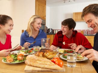 Teenage Family Eating Lunch Together In Kitchen Laughing