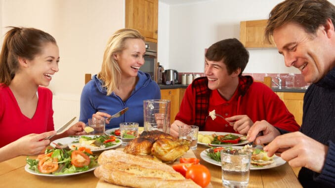 Teenage Family Eating Lunch Together In Kitchen Laughing