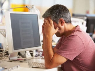 Stressed Man Working At Desk In Busy Creative Office On Computer