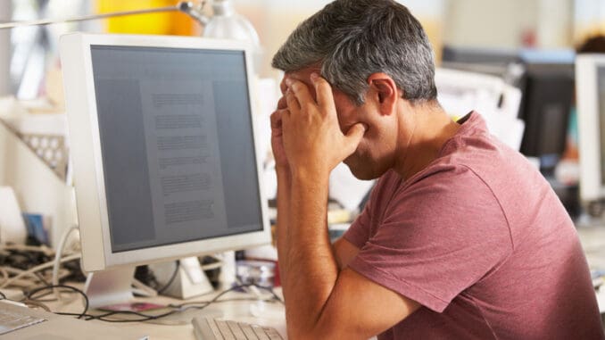 Stressed Man Working At Desk In Busy Creative Office On Computer