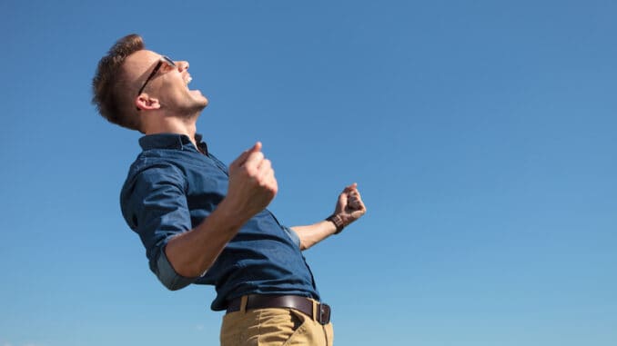 Side view of a casual young man cheering outdoor with a shout while looking away from the camera