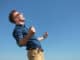 Side view of a casual young man cheering outdoor with a shout while looking away from the camera