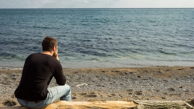 dreamstime_s_34731827 A man sitting on a log looking out to the sea and thinking