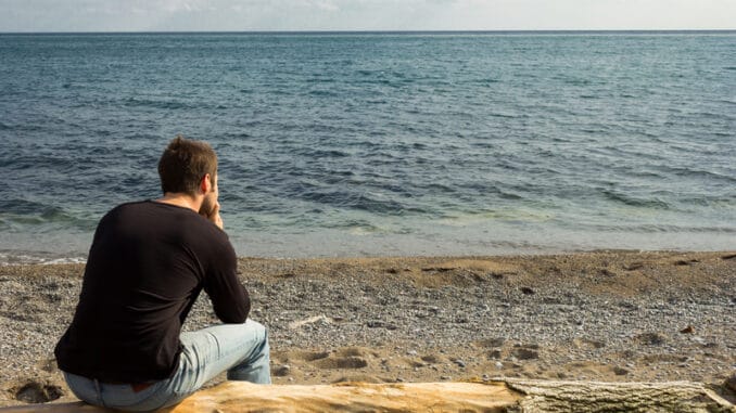 A man sitting on a log looking out to the sea and thinking