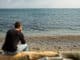 A man sitting on a log looking out to the sea and thinking