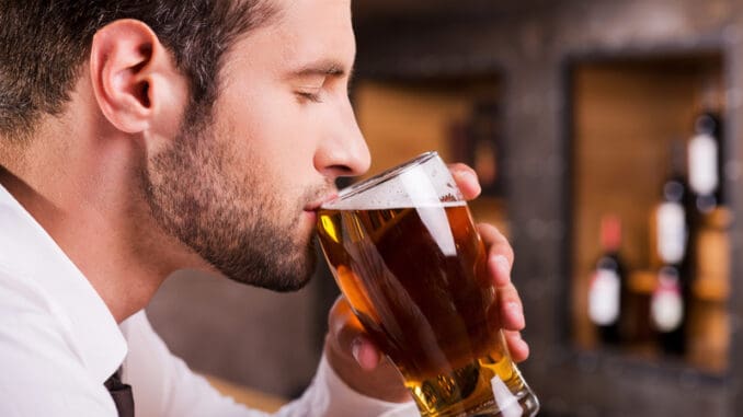 Side view of handsome young man drinking beer while sitting at the bar counter