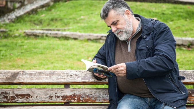Attractive bearded man reading in a big park