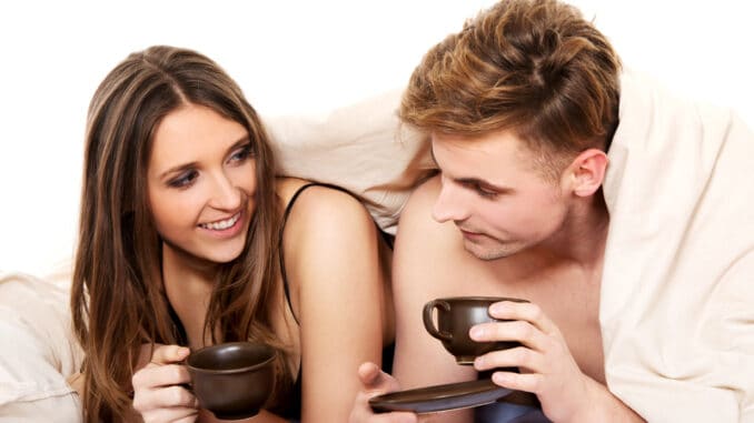 Young happy couple drinking coffee in bed.