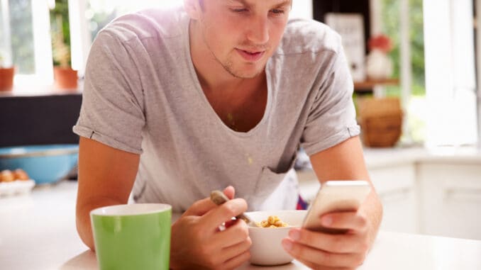 Man Eating Breakfast Whilst Checking Mobile Phone