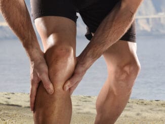 Young sport man with strong athletic legs holding knee with his hands in pain