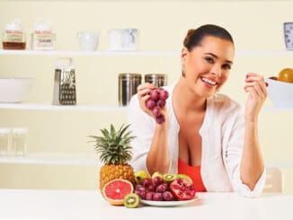Young beautiful woman eating grapes from a fruit bowl in the kitchen