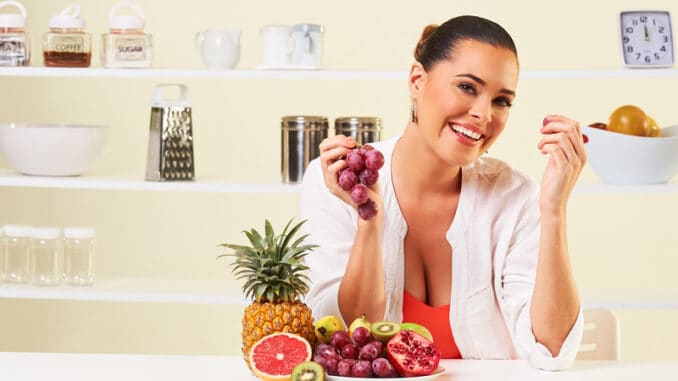 Young beautiful woman eating grapes from a fruit bowl in the kitchen