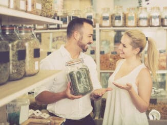 Happy women and men holding glass can with dried herbs in organic shop