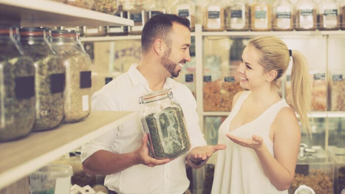 Happy women and men holding glass can with dried herbs in organic shop