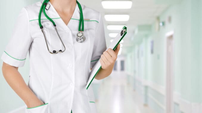 Female medical doctor with clipboard standing over blurry hospital background.