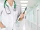 Female medical doctor with clipboard standing over blurry hospital background.