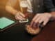 People, leisure and technology concept - close up of man with tablet pc computer drinking beer and eating peanuts at bar or pub