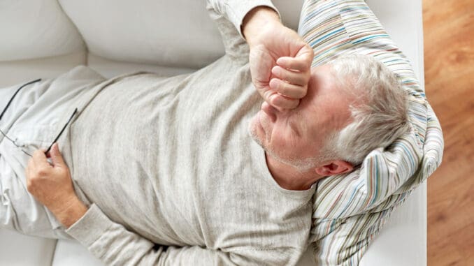 close up of tired senior man lying on sofa at home