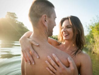 Smiling nude couple hugging in the lake on sunny day