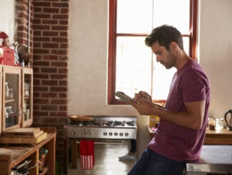 Young man using tablet computer in kitchen, waist up