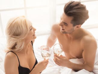 Young couple men and women intimate relationship on bed drinking champagne