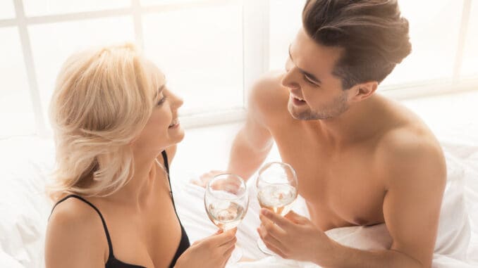 Young couple men and women intimate relationship on bed drinking champagne