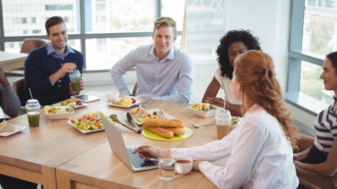 Business colleagues discussing while sitting around breakfast table at office cafeteria