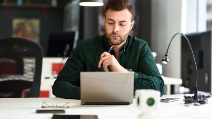 Young man studying with laptop computer on white desk.